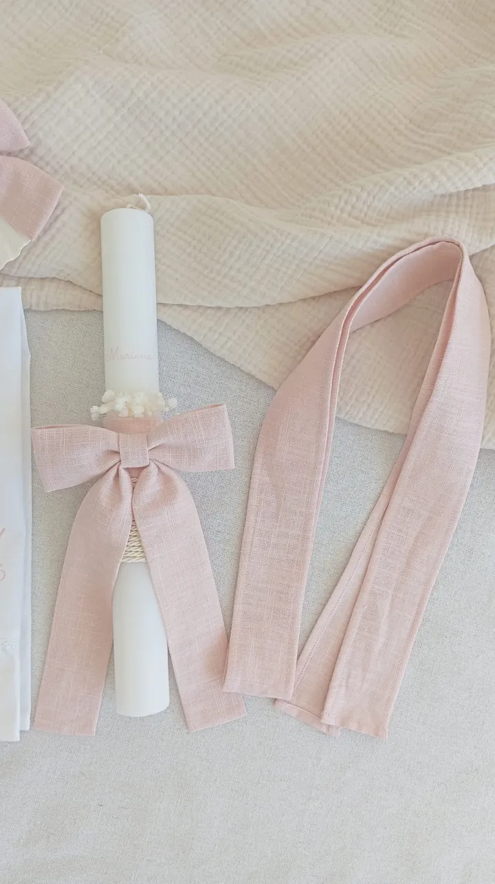 Vela de batismo com laço rosa e, ao lado, o cinto de linho rosa para o vestido, a condizer